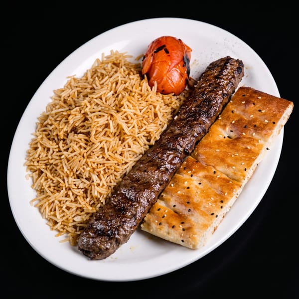 A plate of Persian Kubideh kebab with basmati rice, grilled tomato, and flatbread.