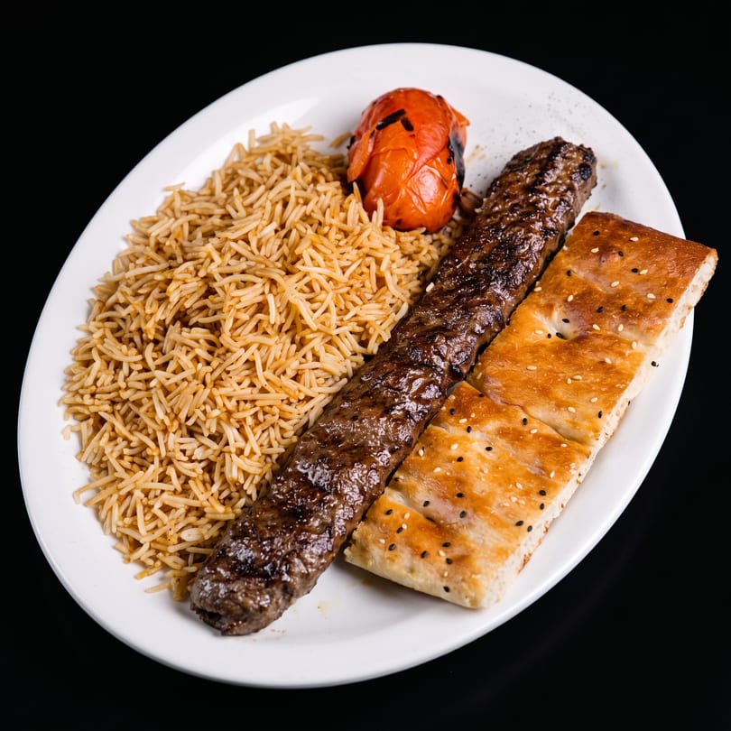 A plate of Persian Kubideh kebab with basmati rice, grilled tomato, and flatbread.