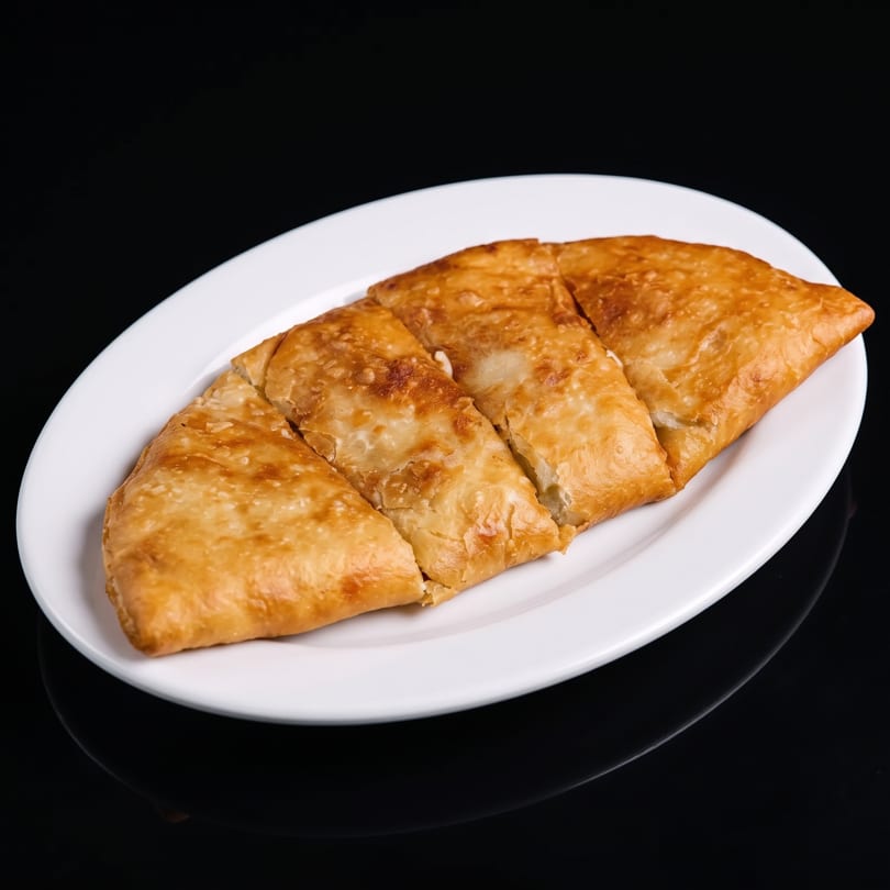 Golden-brown fried flatbread, cut into four pieces, served on a white oval plate.