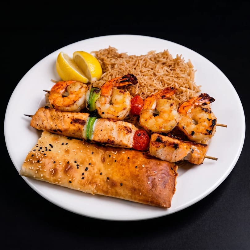 Grilled shrimp and salmon skewers with rice, lemon, and a sesame flatbread on a white plate.