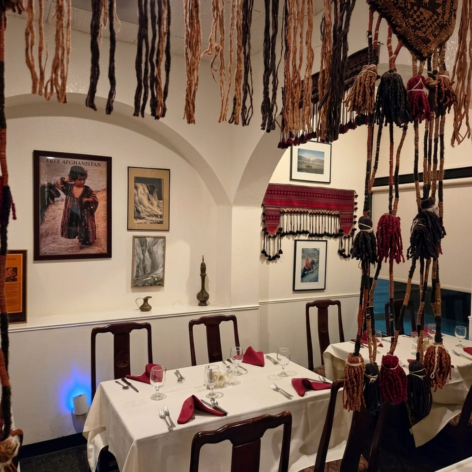 Restaurant dining room with white tablecloths, dark wooden chairs, and Afghan-themed wall decor and ceiling hangings.