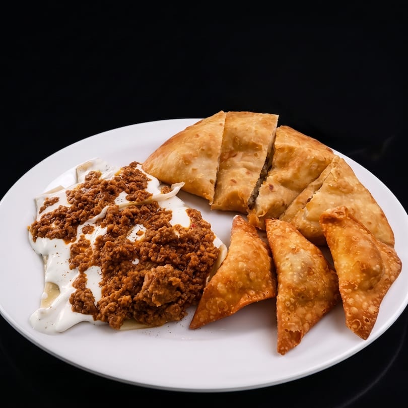 A white plate with fried pastries, one large cut into slices, and a smaller pile of samosas.