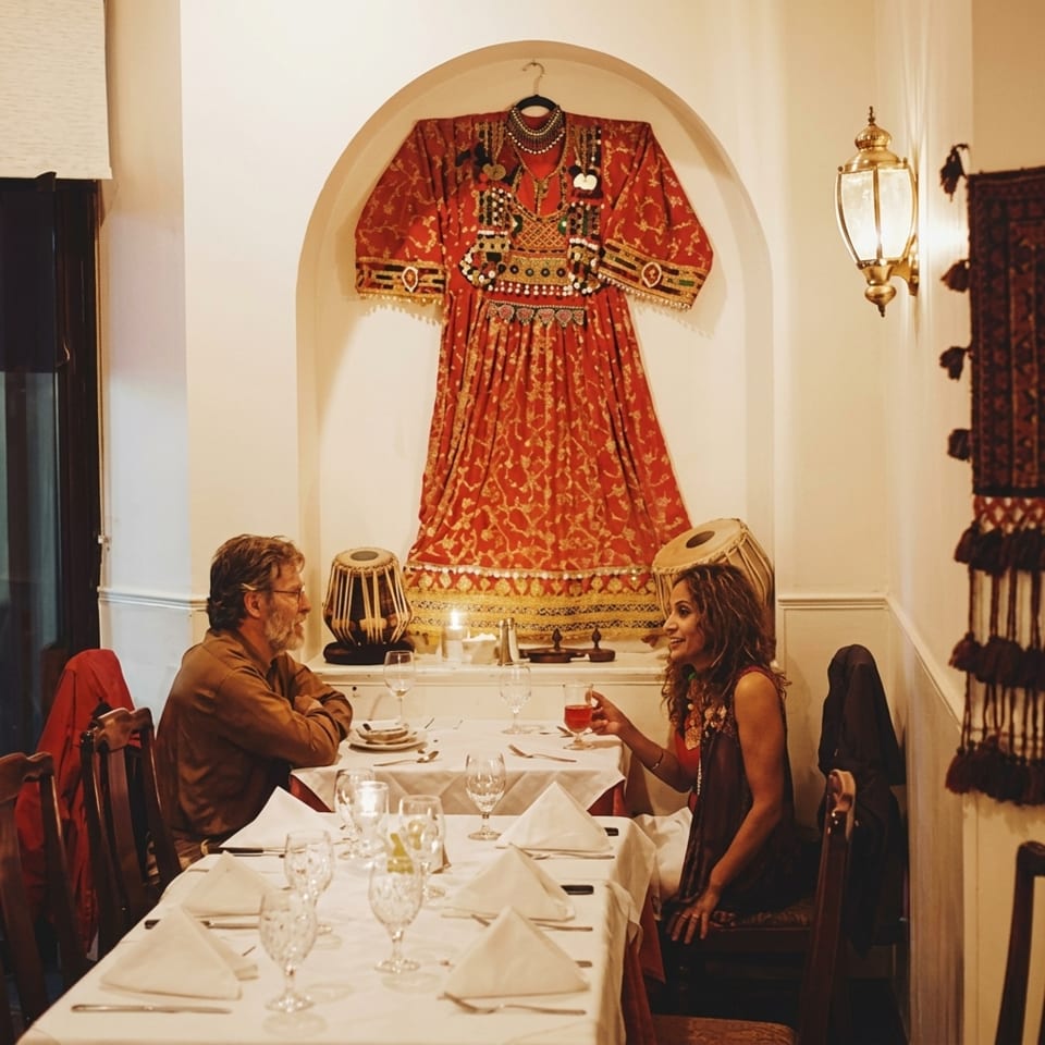 Couple dining in a restaurant with traditional red dress and tabla drums as decor.
