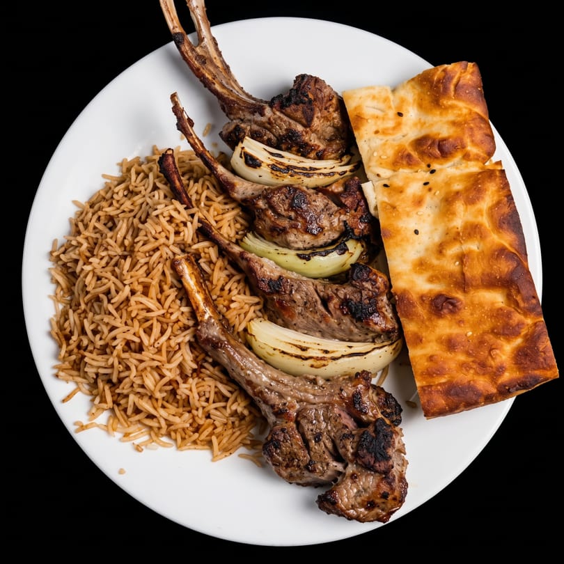 Grilled lamb chops with charred onions, rice pilaf, and flatbread on a white plate.